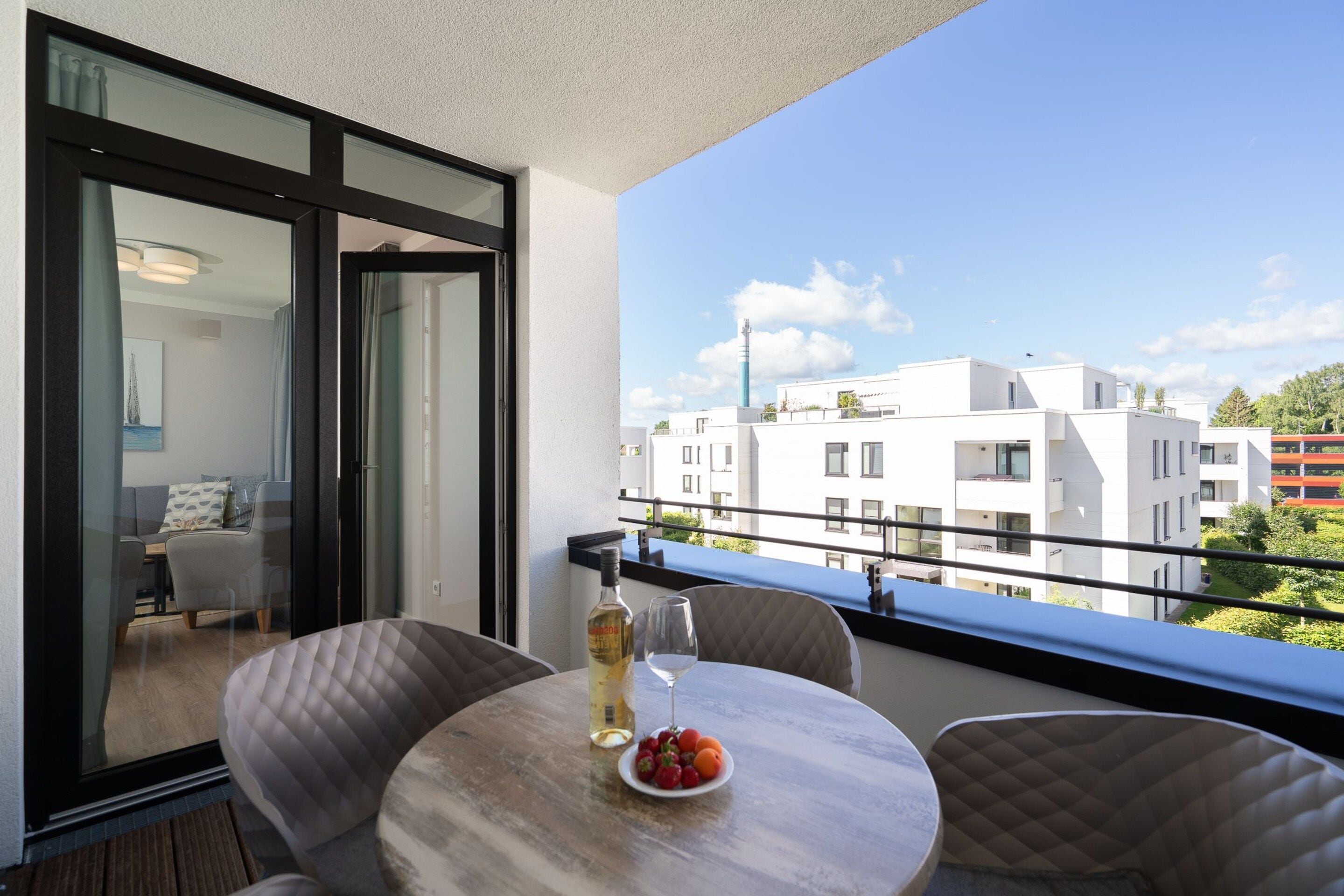 A balcony with a table, chairs, a bottle of wine, and a plate of fruit.