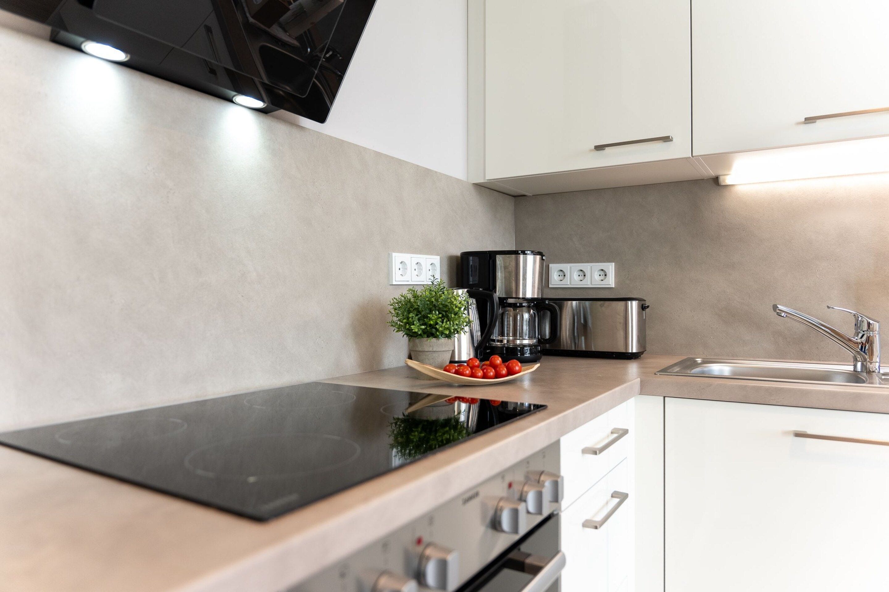A modern kitchen with a black induction cooktop, stainless steel appliances, and a minimalist design.