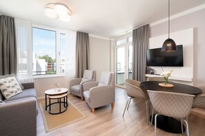 A modern living room with a sofa, armchairs, a coffee table, and a dining area with a TV mounted on the wall. - Modern Holiday Apartment With Sunny Loggia (Lübeck)