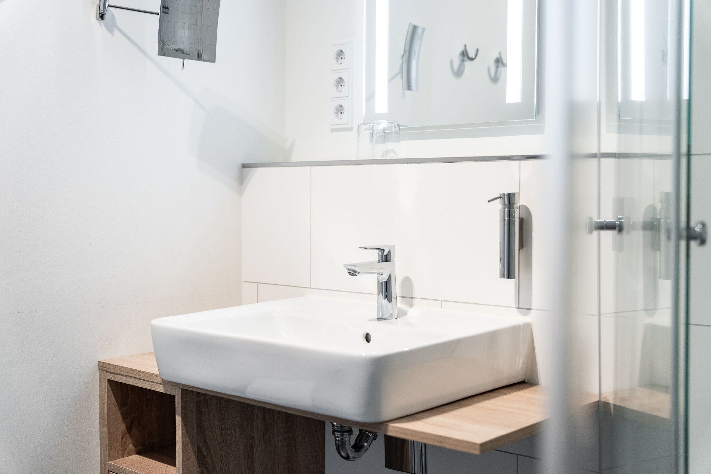 Un baño moderno con un lavamanos blanco, grifo cromado y tocador de madera.