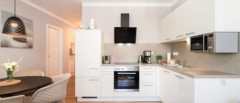 Una cocina moderna con armarios blancos, horno empotrado, microondas y cafetera.