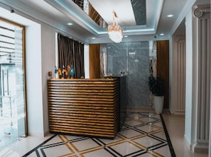A reception area with a modern reception desk, a chandelier, and a marble wall. - Art Plaza Tashkent (Tashkent)