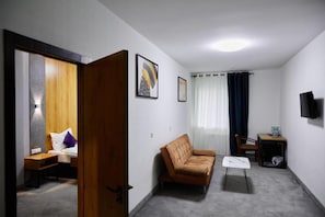 A room with a bed, a sofa, a small table, a TV mounted on the wall, and a door leading to another room. - Art Plaza Tashkent (Tashkent)
