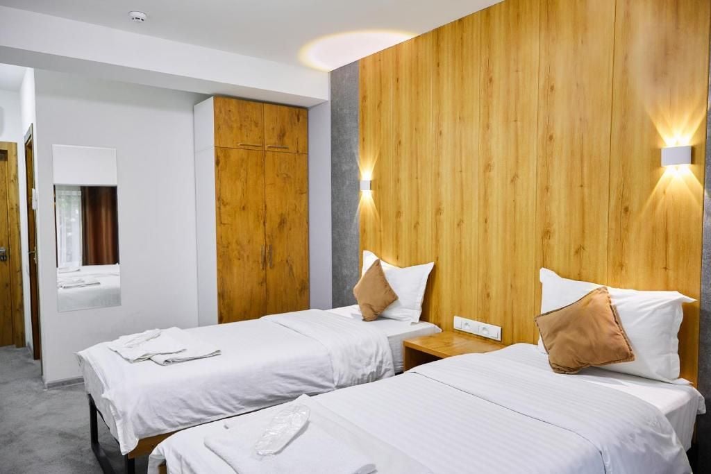 A hotel room with two beds, wooden paneling on the walls, and a mirror above the left bed.