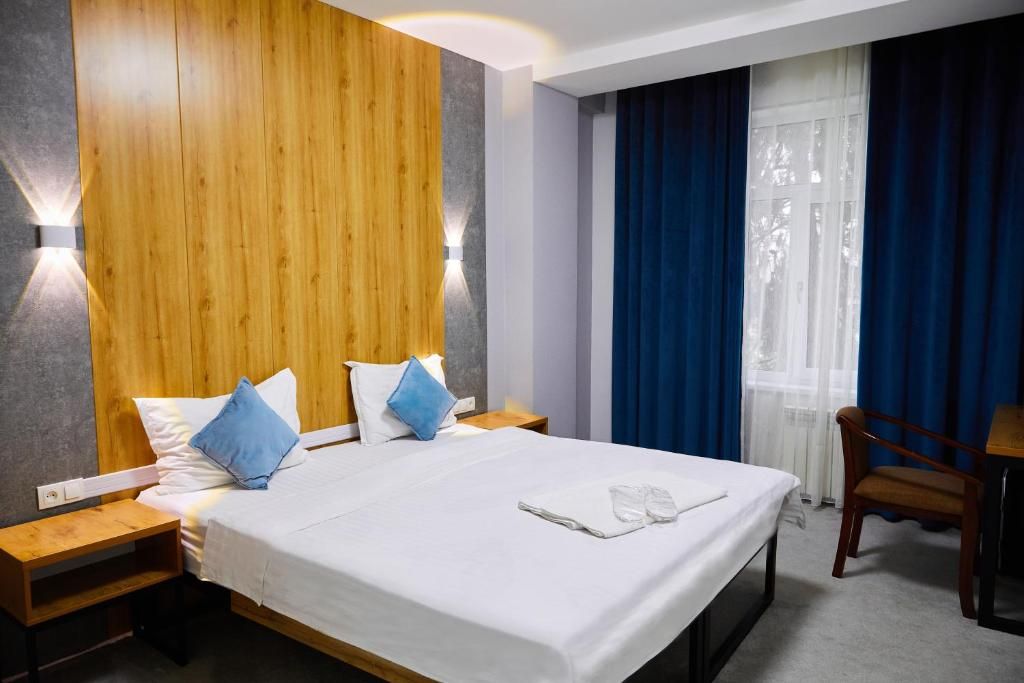 Une chambre d’hôtel avec un grand lit, deux tables de chevet, une tête de lit en bois, un coin salon avec un fauteuil et une fenêtre avec des rideaux.