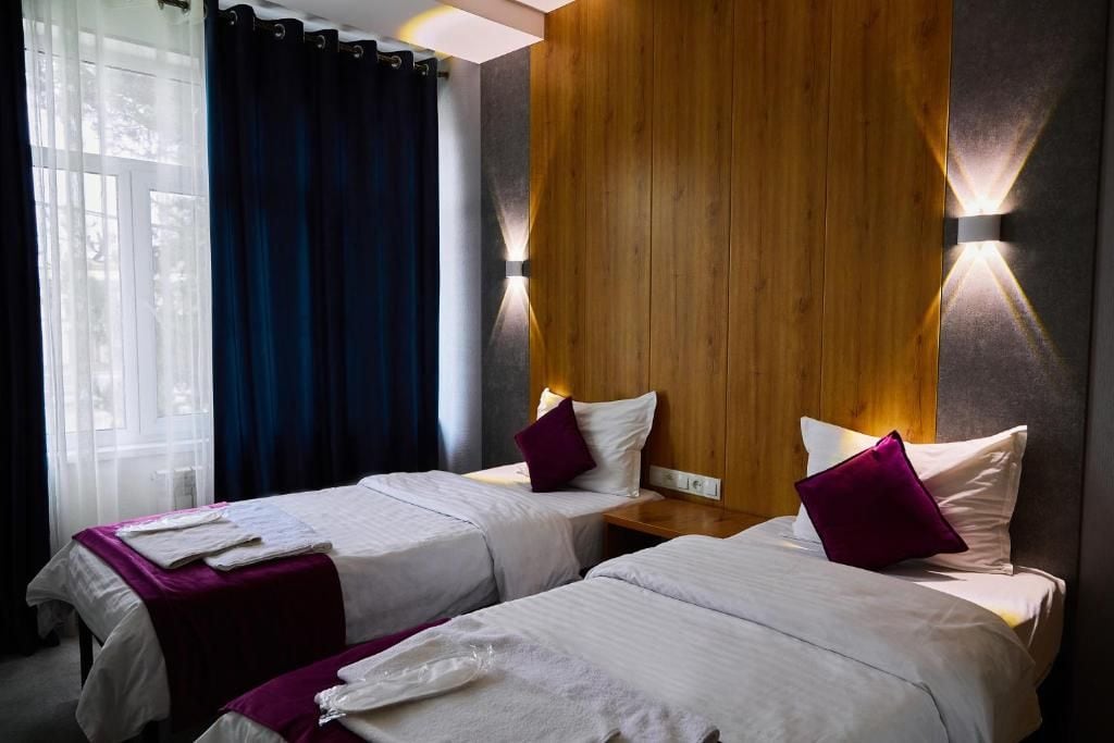 A hotel room with two beds, a wooden accent wall, and a window with curtains.