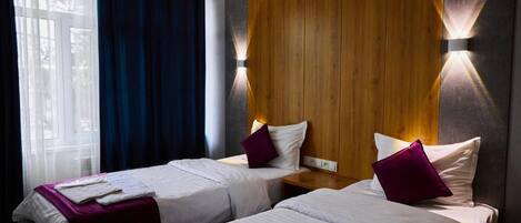 A hotel room with two beds, a wooden accent wall, and a window with curtains.