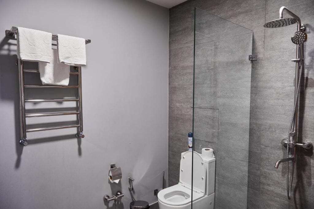 Et moderne badeværelse med en glasbrusekabine, toilet og et håndklædetørrestativ med to håndklæder.