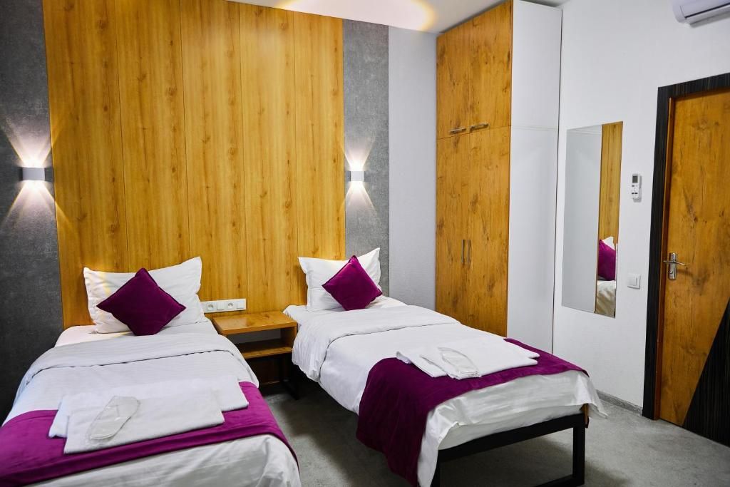 A hotel room with two beds, wooden paneling on the wall, a nightstand, and a mirror.