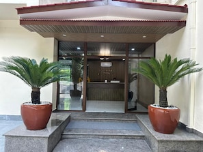 A reception area with a wooden reception desk, two potted palm plants, and a glass entrance. - GawaiLing Residency (Samtse)