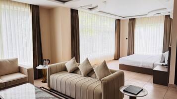 Een hotelkamer met een bank, een bed, een bijzettafeltje en een klein nachtkastje.