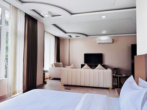 Habitación de hotel con cama, sofá, televisor y ventana con cortinas.
