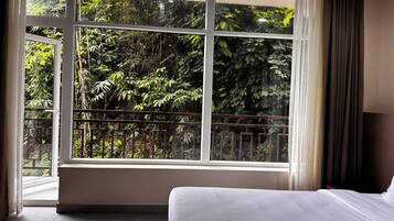 Ein Hotelzimmer mit großem Fenster, einem Bett und Blick auf dichtes Grün.
