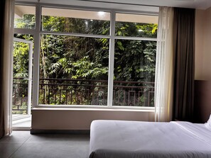 Habitación de hotel con un ventanal grande, una cama y vistas a una vegetación densa.
