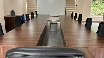 Un salón de conferencias con una larga mesa, sillas, una pantalla de proyector y vistas al exterior con zonas verdes.