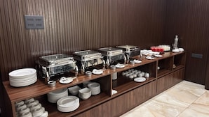 Een buffetopstelling met meerdere aanzitpunten, inclusief schalen en kommen, en een verscheidenheid aan gerechten en bestek.