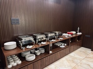 A buffet setup with multiple serving stations, including trays and bowls, and a variety of dishes and utensils. - GawaiLing Residency (Samtse)