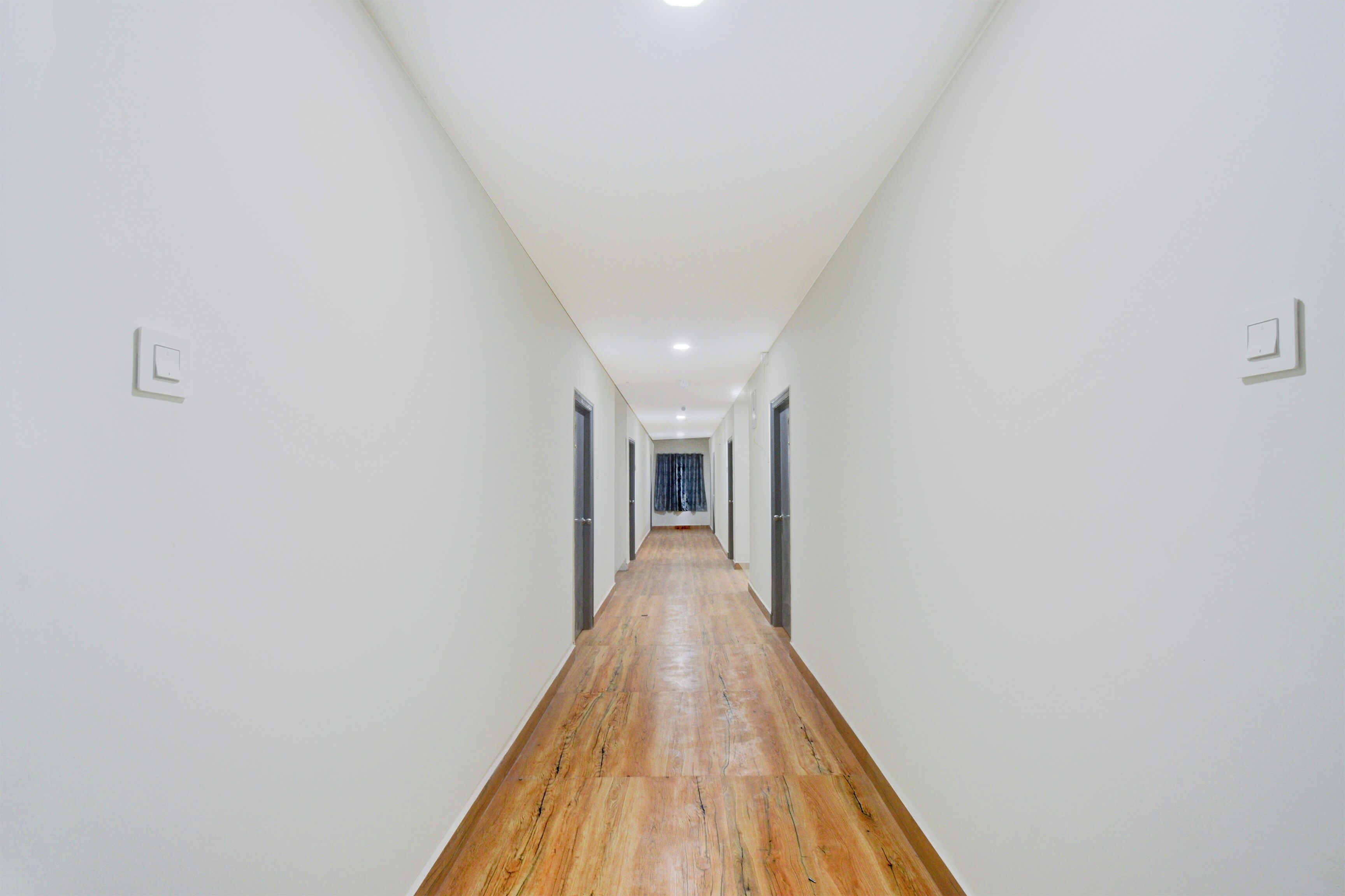 A long, narrow hallway with white walls and wooden flooring, leading to a door at the end.