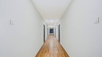 A long, narrow hallway with white walls and wooden flooring, leading to a door at the end.