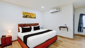 Une chambre d’hôtel avec un grand lit, une table de chevet avec une lampe, un appareil de climatisation, une étagère fixée au mur et un tableau.