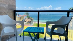 Ein Balkon mit zwei weißen Stühlen und einem kleinen Tisch mit Blick auf einen Strand und das Meer.