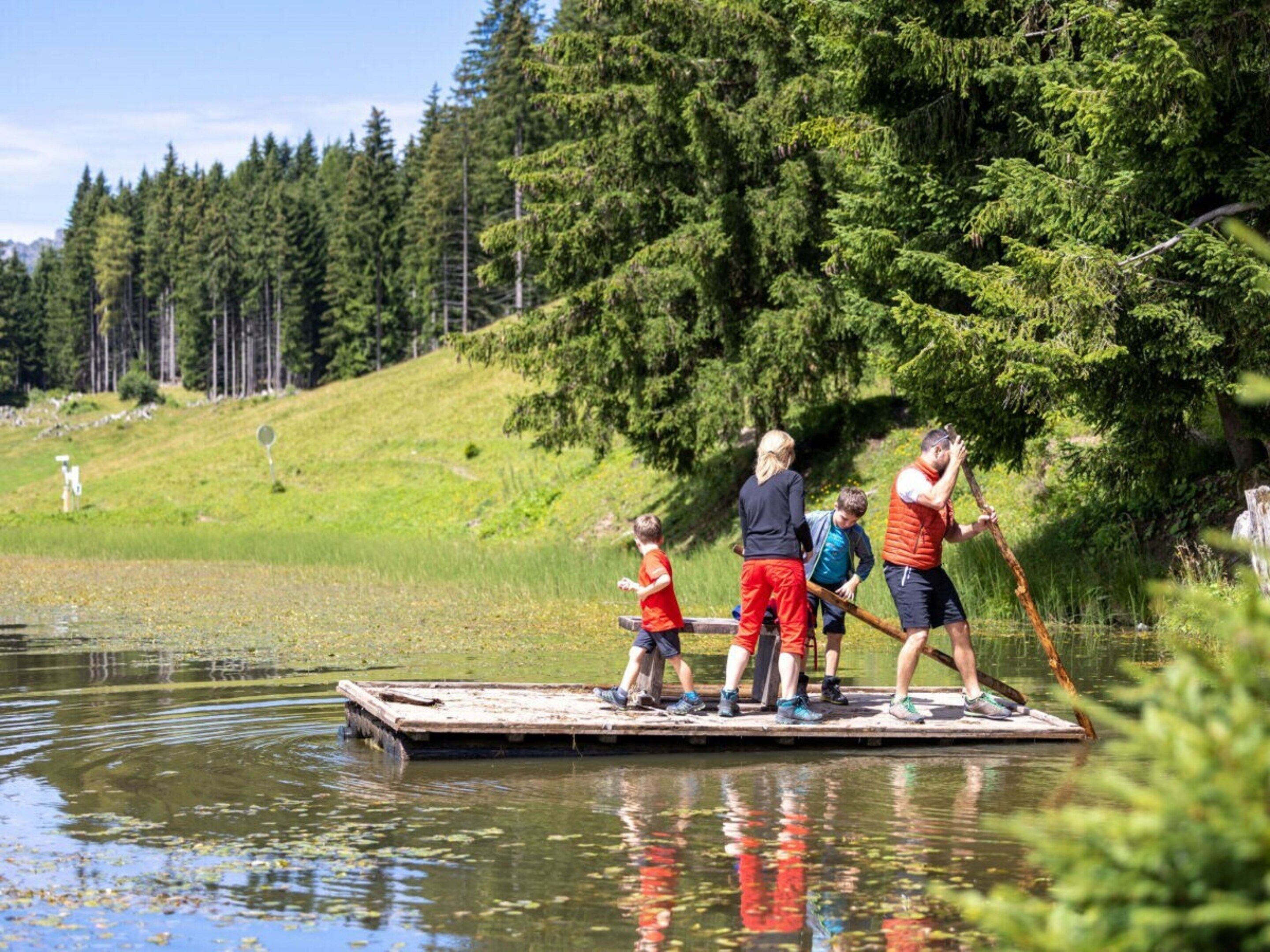 A group of people on a wooden dock by a lake surrounded by trees.
