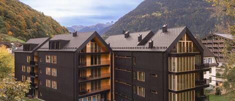 A multi-story building with balconies, a swimming pool, and a mountainous backdrop.