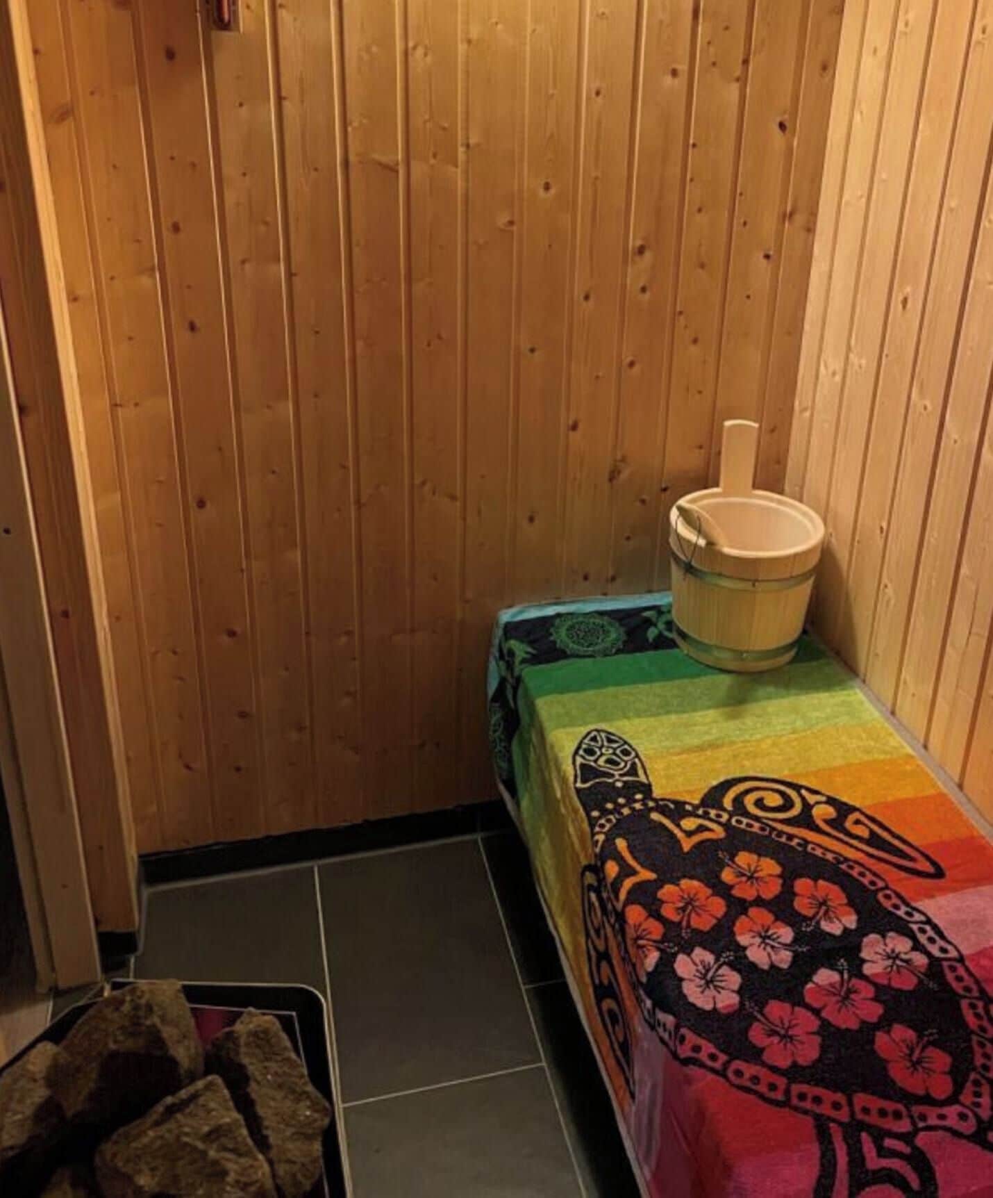 Pequeno salão de sauna de madeira com um banco e um balde.