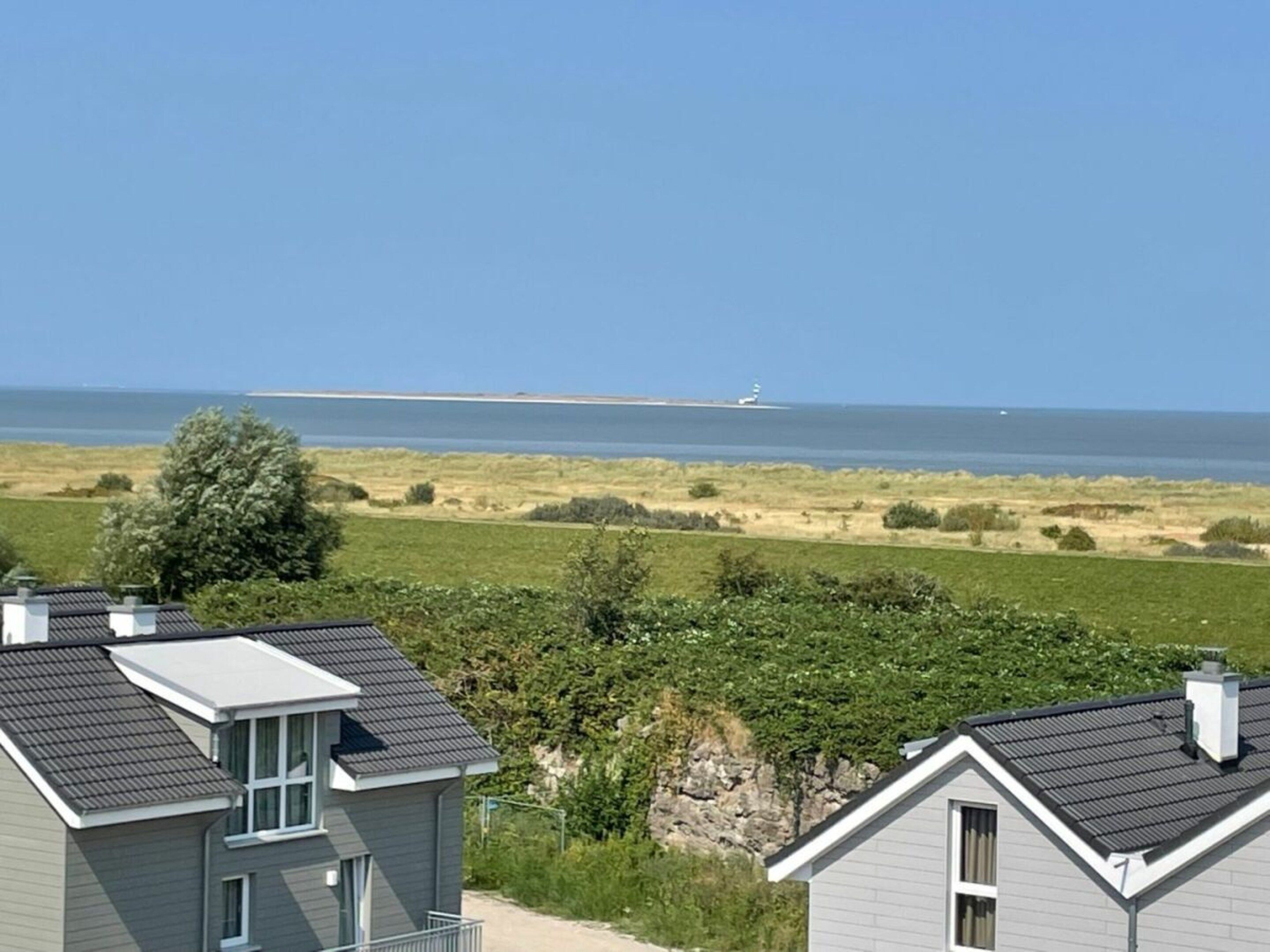 A residential area with houses, a view of the sea, and a distant lighthouse.