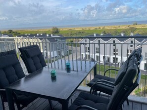 Ein Balkon mit Tisch und Stühlen, der auf ein Wohngebiet mit Häusern und Blick aufs Meer blickt.