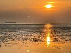 Un coucher de soleil sur une mer calme, avec un navire à l'horizon.