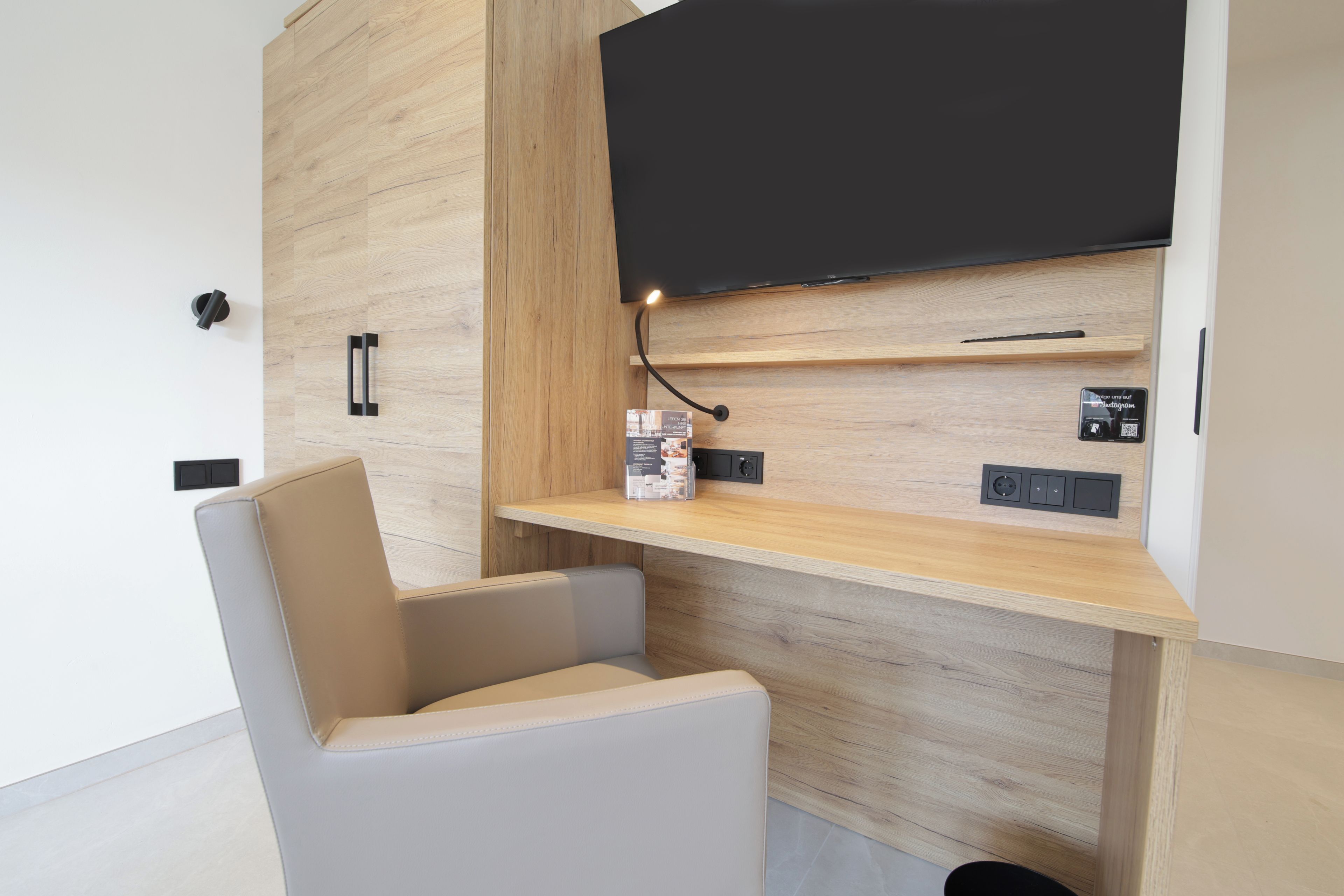 Ein modernes Wohnzimmer mit integriertem Fernseher, einem Holzregal und einem bequemen Sessel.