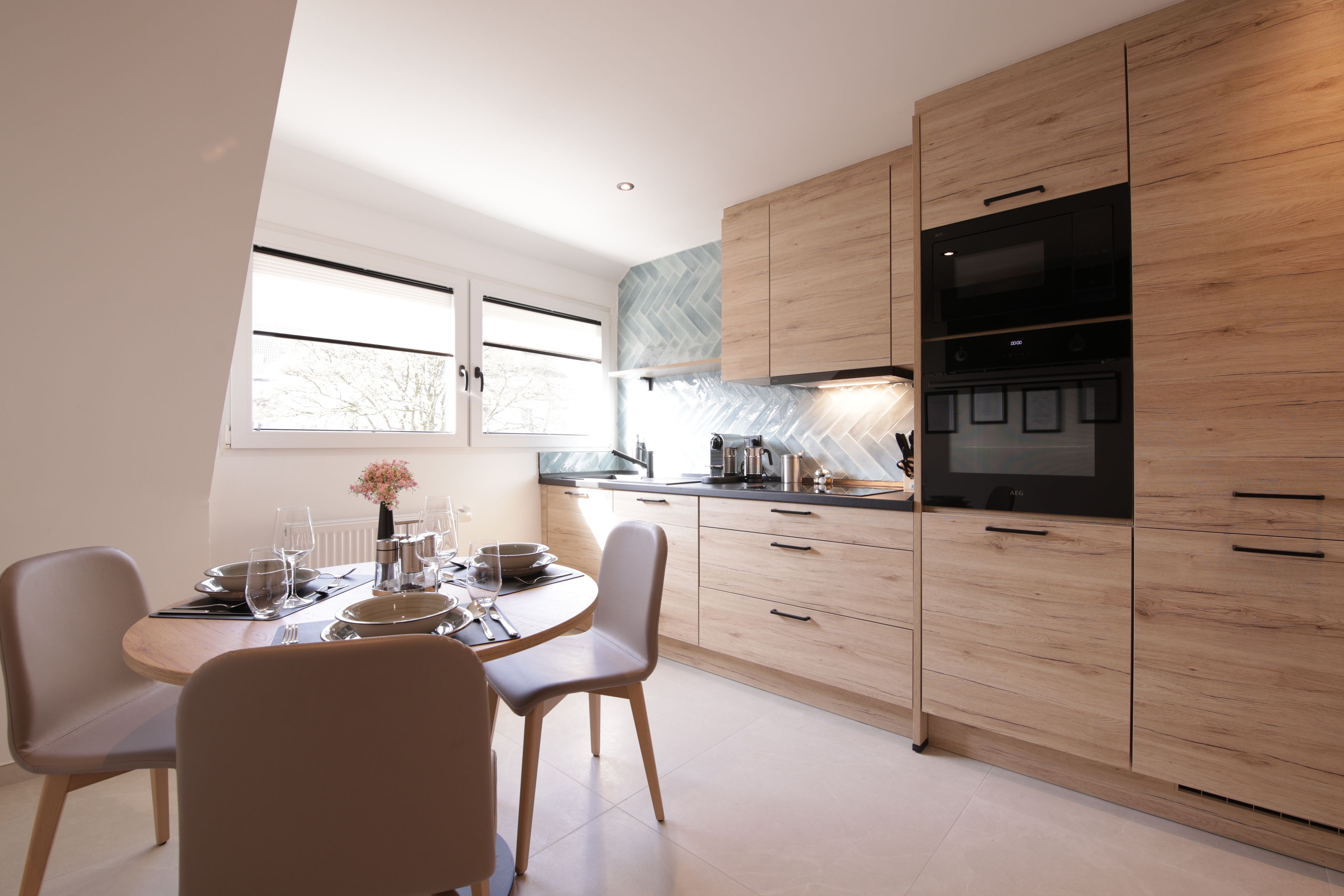 A modern kitchen with wooden cabinets, a dining table set for four, and a large window.