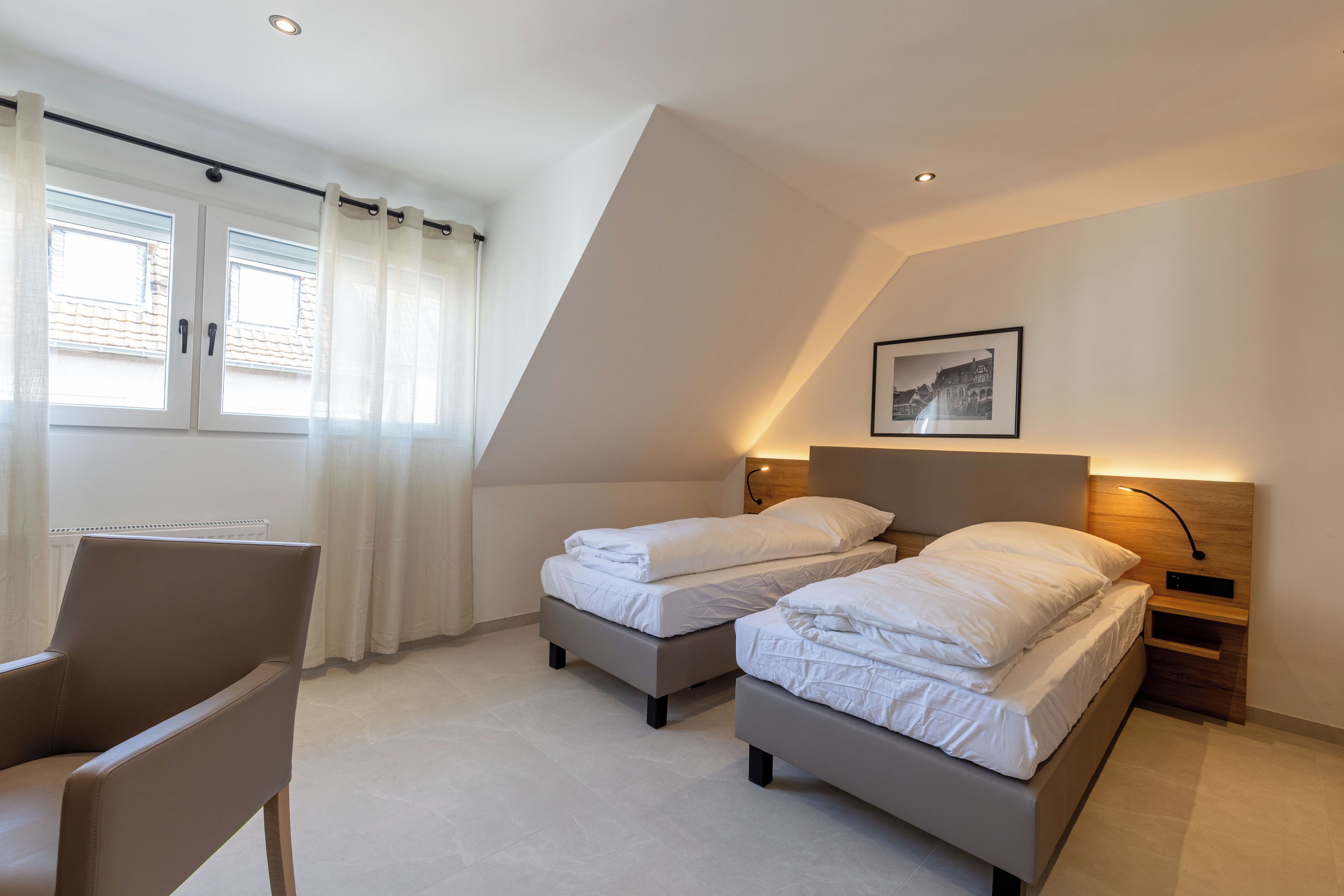Ein modernes Schlafzimmer mit zwei Betten, einem Sessel und einem Fenster mit Vorhängen.