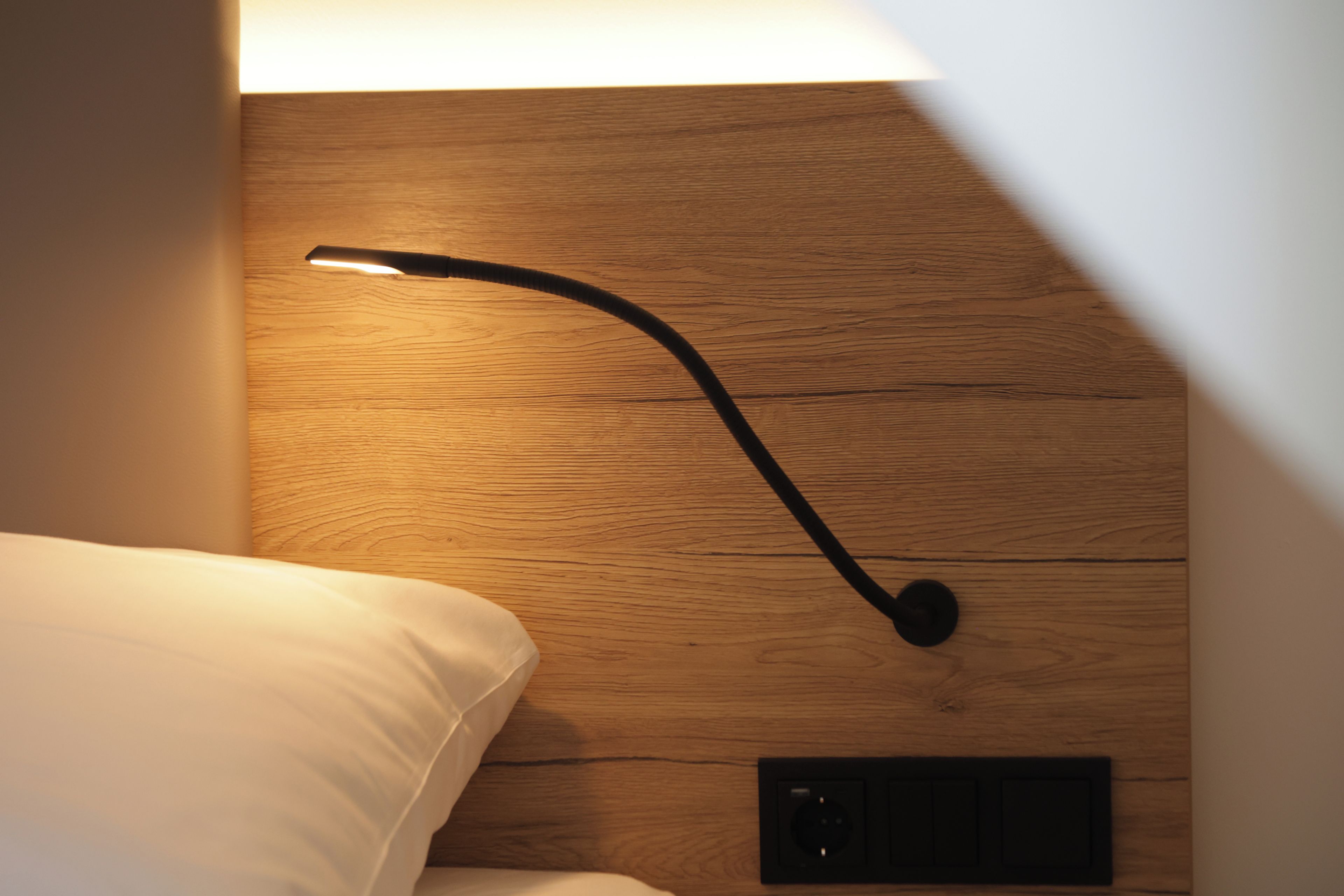 A wooden headboard with a modern bedside lamp and a power outlet.