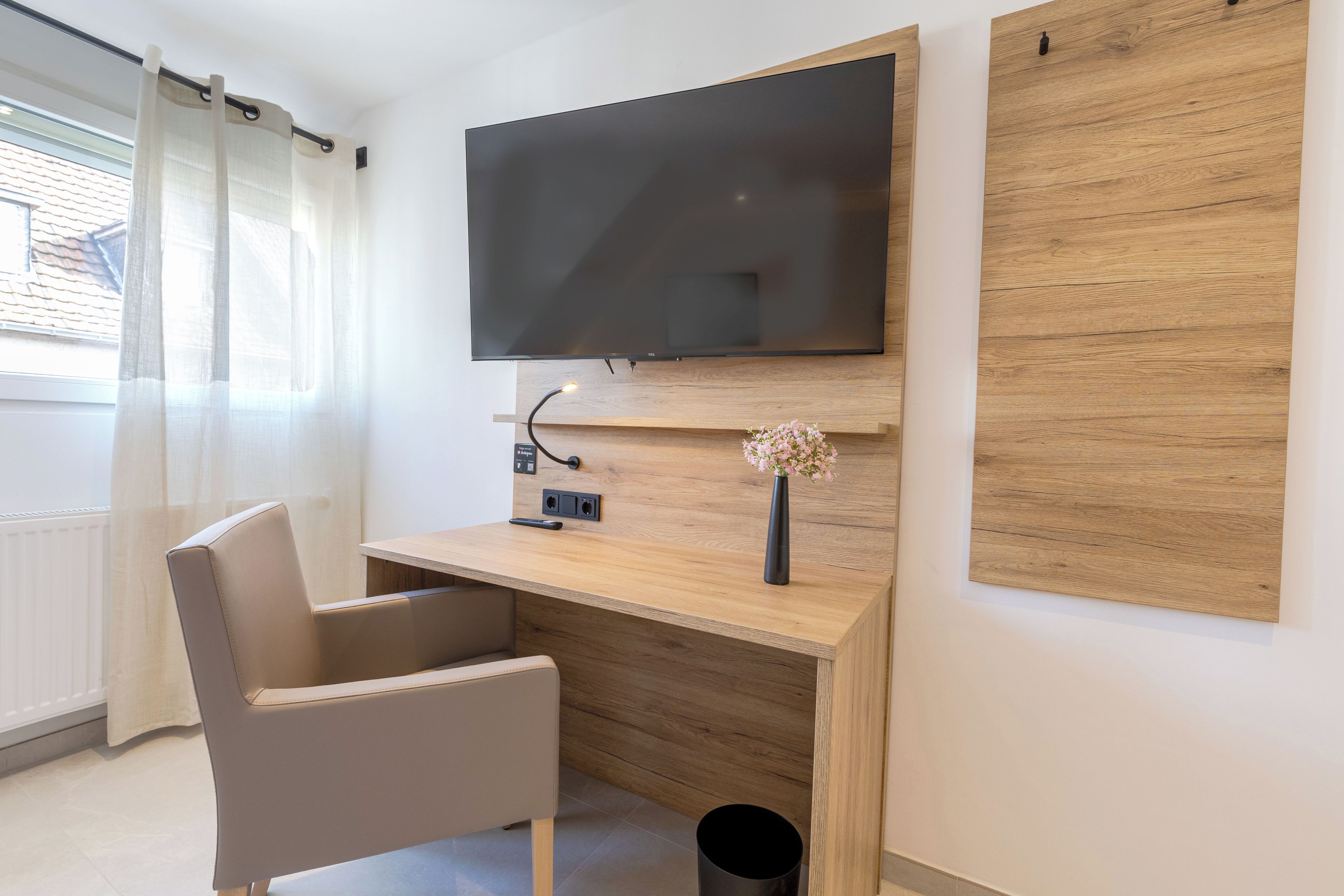 A modern room with a flat-screen TV mounted on a wooden wall, a desk with a vase of flowers, and a chair.