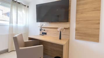 A modern room with a flat-screen TV mounted on a wooden wall, a desk with a vase of flowers, and a chair.