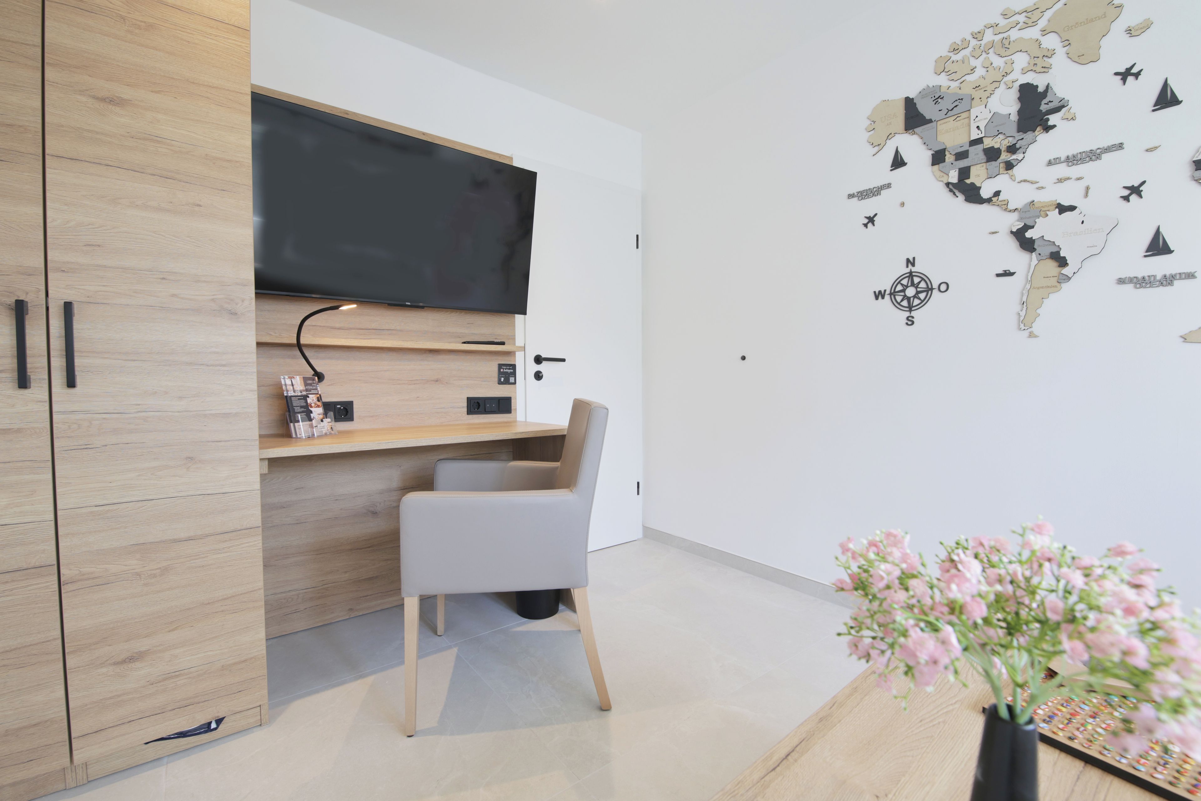 A modern room with a wooden wardrobe, a desk with a flat-screen TV, a chair, and a wall map.