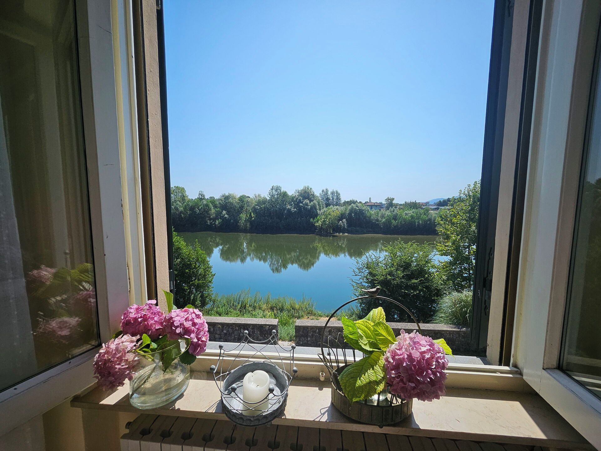 A window view of a calm lake with trees and a clear sky.