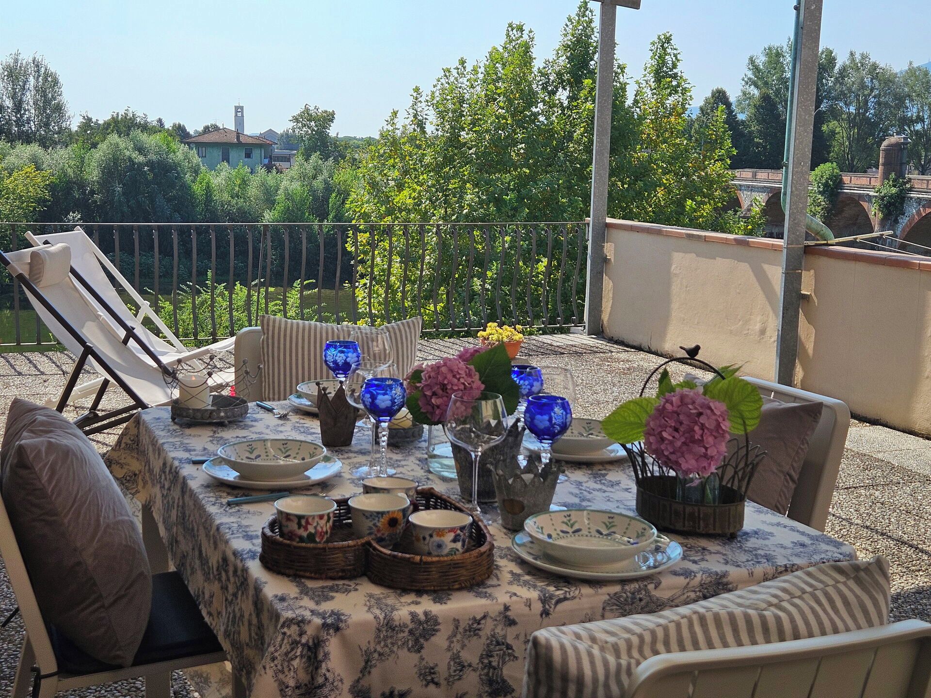 An outdoor dining area with a table set for two, surrounded by chairs, and a view of the cityscape in the background.