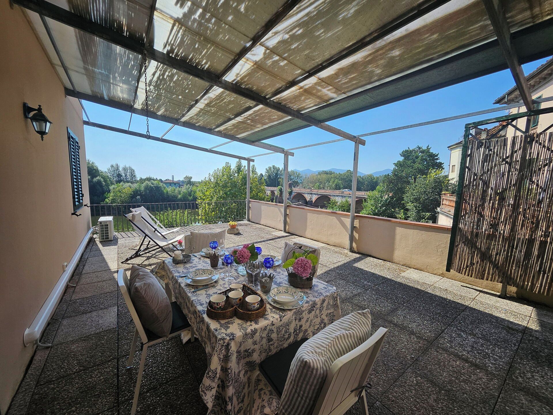 Une terrasse extérieure avec une table dressée pour le repas, entourée de chaises, et un espace abrité offrant une vue sur le paysage.