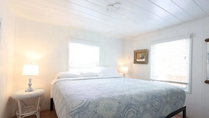 Ein Schlafzimmer mit einem Bett, zwei Nachttischlampen, einem kleinen Tisch und einem Fenster mit Jalousien.