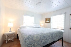 A bedroom with a bed, two bedside lamps, a small table, and a window with blinds.
