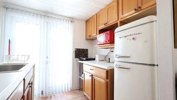 A kitchen with wooden cabinets, a white refrigerator, and a window with curtains.