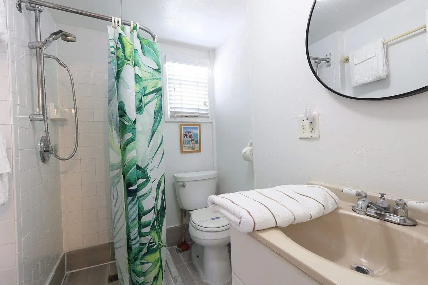 A bathroom with a shower, toilet, sink, and a mirror.