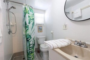 A bathroom with a shower, toilet, sink, and a mirror.
