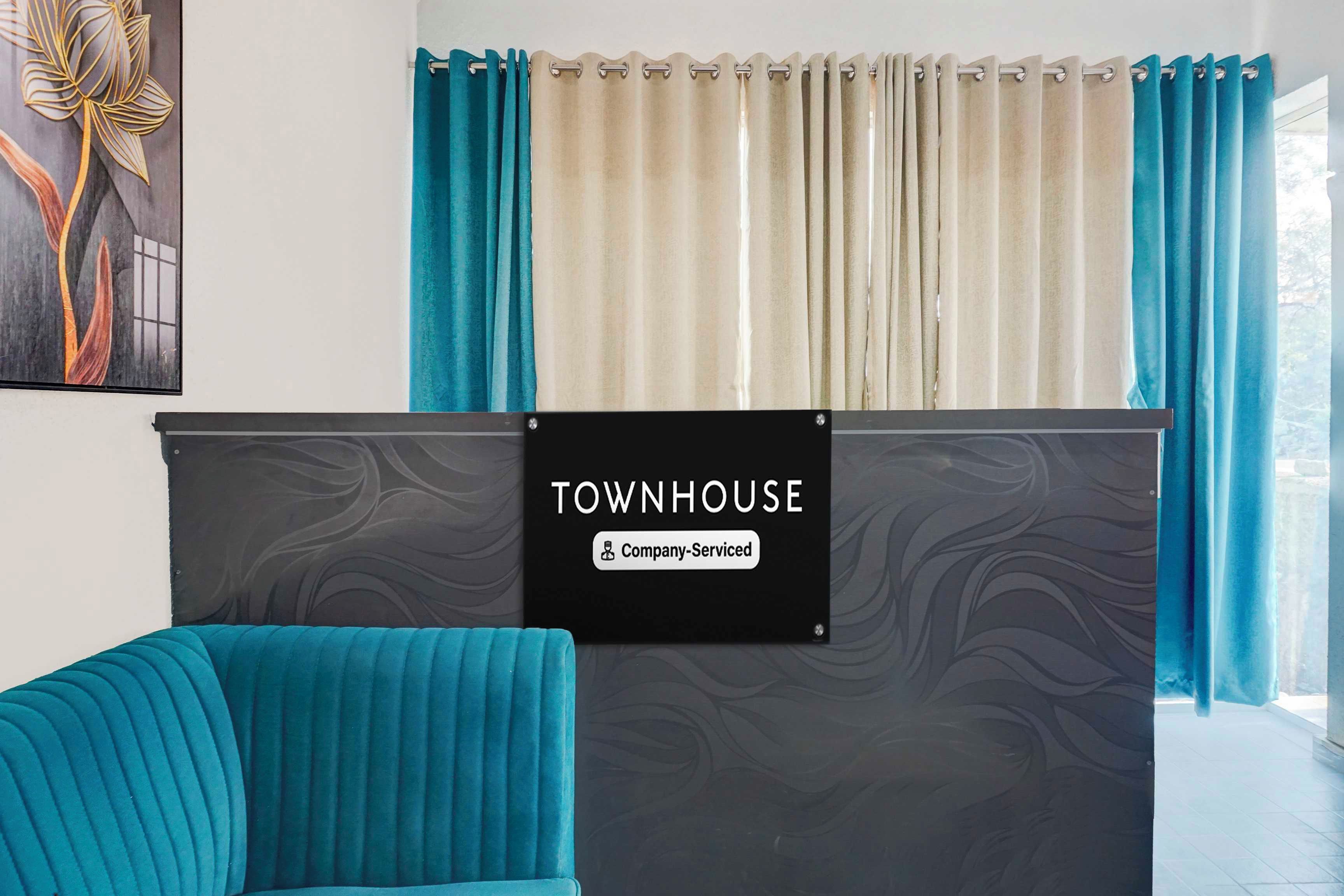 Mostrador de recepción con un cartel que indica 'Company-Serviced' en un interior moderno con cortinas color turquesa y un diseño de pared similar al mármol.