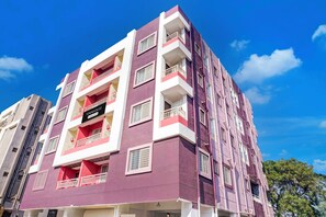 Un edificio residencial de varios pisos con balcones, un letrero que indica que es una propiedad con servicios de empresa, y un cielo azul despejado al fondo.