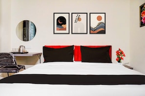 A hotel room with a bed, a desk, a chair, a round mirror, and three framed artworks on the wall. - Townhouse Oak Sankaramatam Road (Visakhapatnam)