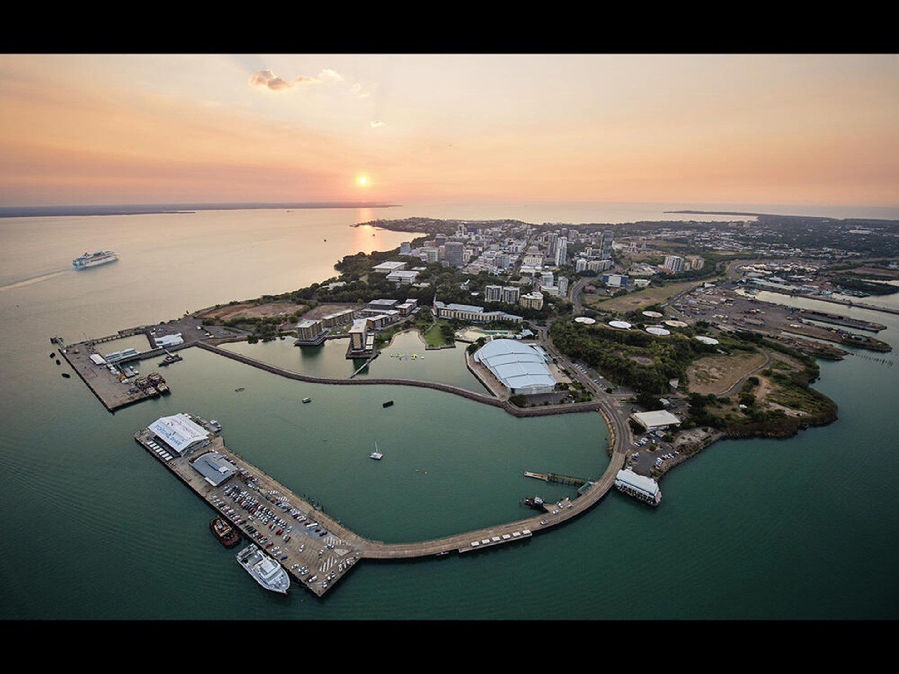 An aerial view of a coastal city with a marina, buildings, and a sunset.